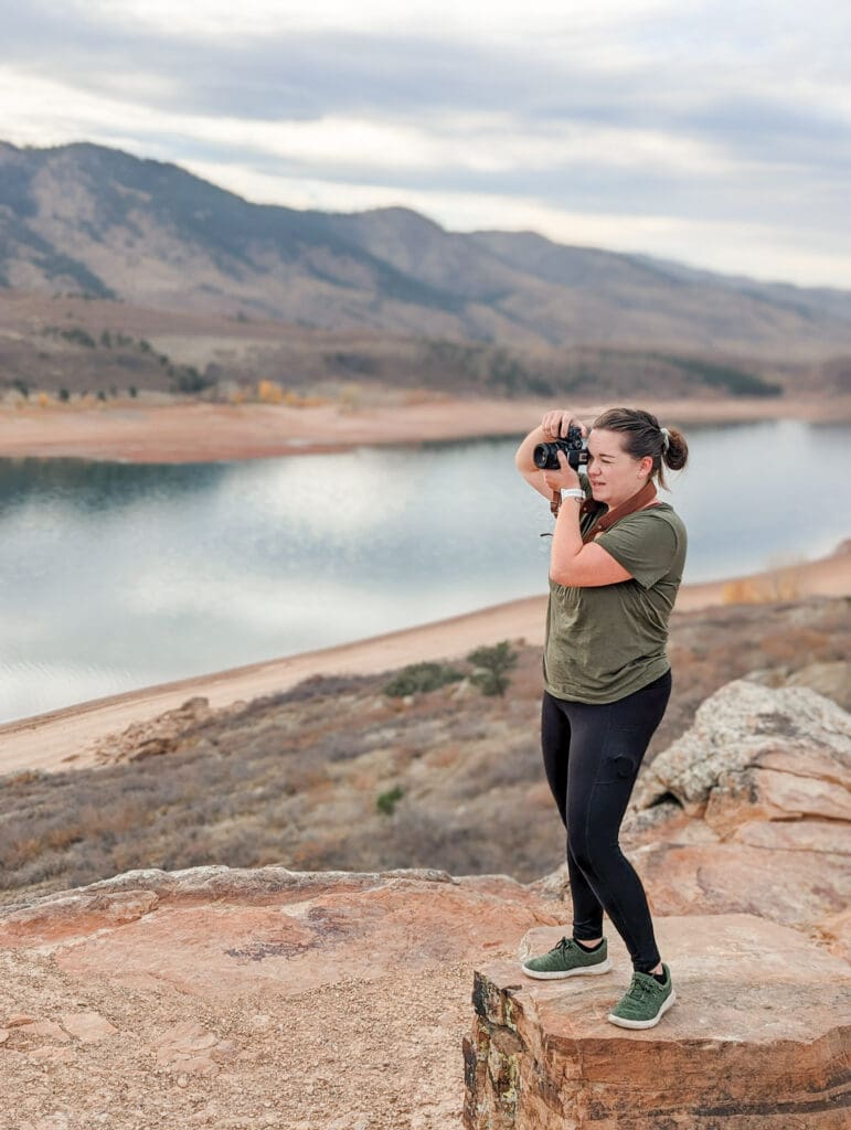 Woman stands on rock overlooking a cliff edge to take a photo | How to tell your brand’s story