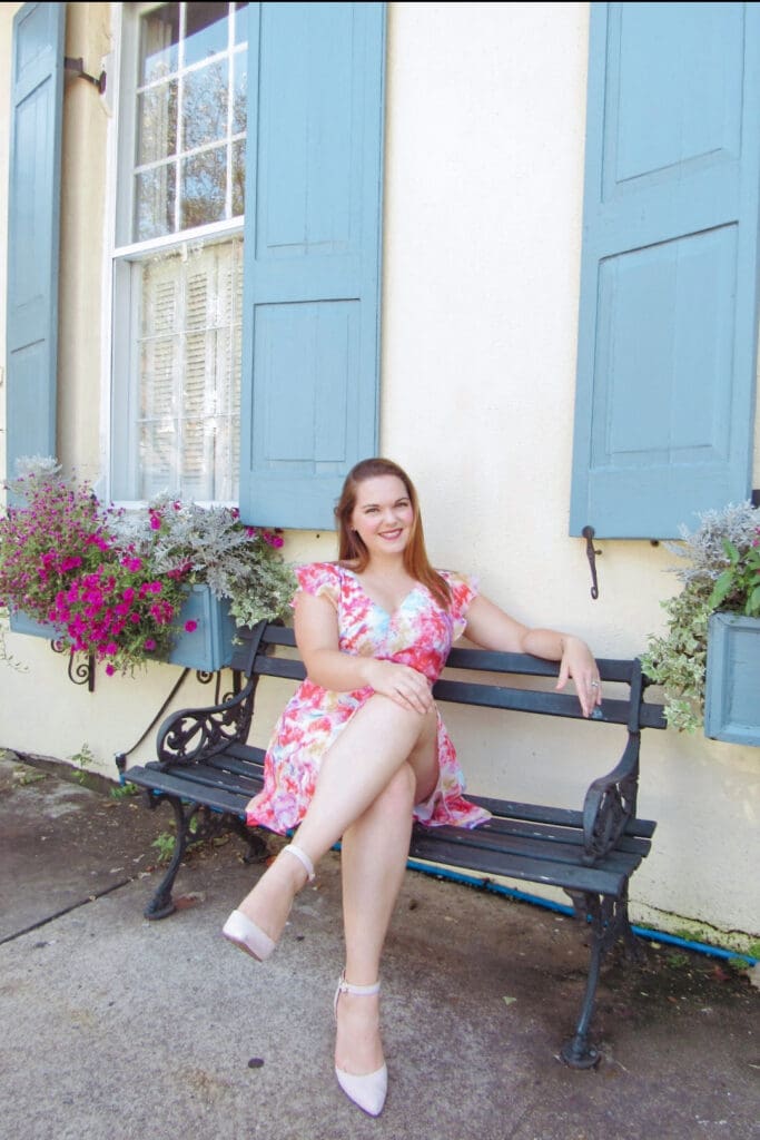 Woman in a colorful dress sits on a bench in front of a colorful building with window boxes full of flowers | How to tell your brand’s story