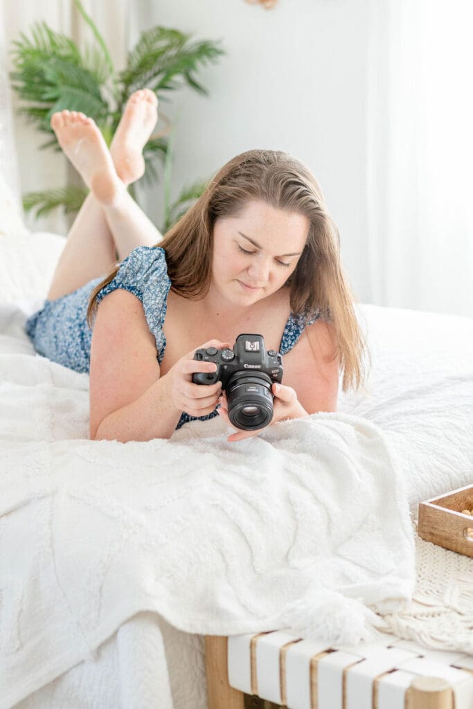 Woman lies on bed looking at screen on back of camera | What to Wear for Your Brand Photos