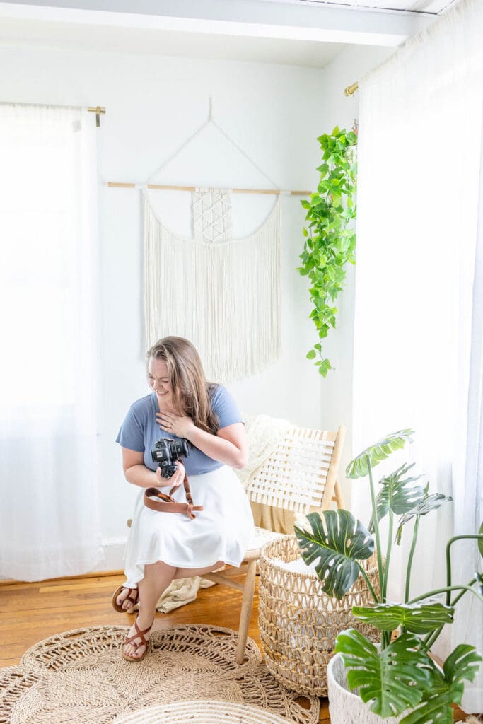 Woman sits on a chair laughing while holding a camera | What to Wear for Your Brand Photos